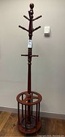 Full view of the tall wooden coat rack showing hooks and umbrella stand base.