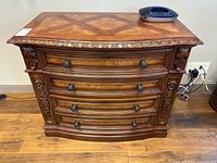 Front view of antique style file cabinet showing four curved drawers with carved floral details and metal knobs.
