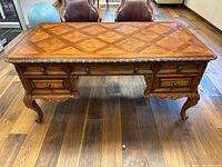 Front view of desk showing parquet veneer top, carved apron, drawers and bail pulls.