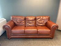 Front view of cognac leather sofa with three cushions and brass studs