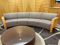 Curved sofa front view showing grey and cream patterned upholstery and Birds Eye maple wood arms on both ends.