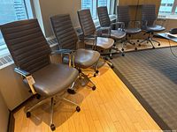 Six grey vinyl upholstered adjustable office chairs arranged in row under windows