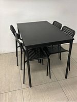Front angle of the black IKEA Sandsberg rectangular kitchen table with four matching black perforated chairs surrounding it.