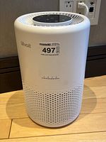 Front view of white cylindrical Levoit air purifier with MaxSold lot label attached, showing exterior perforations and overall condition.