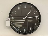 Front view of the modern black wall clock showing clear white numerals and minute markers with white hands on a black face, encased in a black round frame.