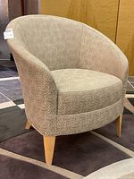 Front angle view of one beige fabric tub chair showing upholstery and wooden legs.
