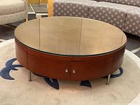 Round mahogany stained wood veneer coffee table with removable glass top, two small doors visible, situated on a circular area rug.