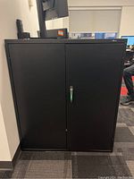 Front view of black metal cabinet with closed doors and keys in lock