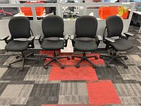 Front view of four black Steelcase Leap chairs in a row on office carpet