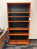 Full frontal view of tall wood veneer bookshelf with six shelves and black back panel.