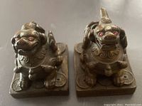 Front view of two bronze Foo Dogs showing red gemstone eyes and detailed facial features.