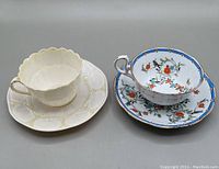 Top view of both teacup and saucer sets side by side showing the Belleek shell motif cup and saucer on left and the Royal Albert Eden floral cup and saucer on right.