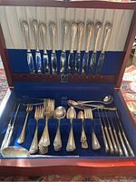 Full view of silverware in wooden storage case showing knives, forks, spoons, serving utensils with patterned handles.
