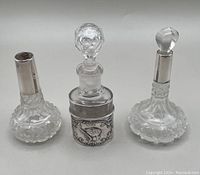 Frontal view showing three cut glass perfume bottles with silver collars and stoppers, arranged side by side on a white background.