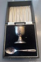 Silver plated egg cup and matching spoon in black fitted box with satin lined lid and velvet base.