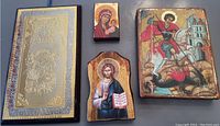 Four wooden icons including two of Mary and baby Jesus, one of Jesus, and one of St. George slaying the dragon, displayed on a table.