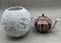 Overall view of the white porcelain vase with embossed floral patterns next to Japanese Imari teapot