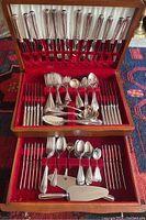 Open two-tier wooden presentation case lined in red velvet showing full flatware service and serving pieces.
