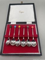 Boxed set of six EPNS coffee spoons held in red velvet slots inside a hinged box with white satin under lid, showing all spoons neatly aligned.