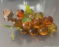 Top and side view showing cluster of amber and yellow lucite grapes attached to driftwood, with artificial green leaves. One grape shows dark/burnt internal spot.