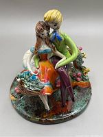 Front angle showing colorful couple sitting on well base with flower basket and vibrant glaze.