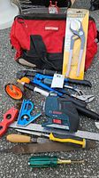 Overview of Craftsman bag, IPS Wonder Plier new in packaging, Lufkin measuring wheel, Bosch laser level, combo square, hand saw, files, and screwdrivers.