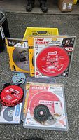 Photo showing multiple circular saw blades from Diablo and DeWalt, including two blades in original packaging and others used with visible teeth, along with a yellow plastic crate.