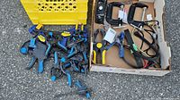 Variety of blue and black spring clamps, bungee cords, Mastercraft C-clamps in a cardboard box with other clamps visible outside the box