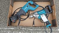 Photo showing both Makita tools in a cardboard box, the reciprocating saw and the hand mixer/drill with visible cords and handles
