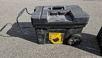 Full view of black Stanley Promobile tool chest with handle and wheels outside on pavement.