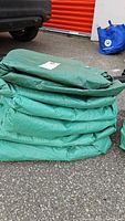 Stack of six green polyethylene tarps folded on ground with visible wear and dirt.