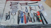 Wide view of the complete hand tools lot arranged on a white surface, showing various pliers, wrenches, bolt cutter, and other tools in used condition.