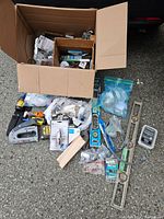 Overview of full box containing an assortment of tools and hardware items including staple gun, levels, screws, anchors, hinges, and packaging.