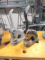 Two vintage corporate embossing seals placed on a wooden workbench, showing both items side by side.