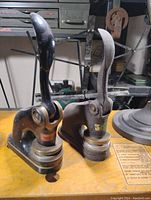 Two vintage corporate embossing seal presses, one black painted metal and one rusted metal, placed on a wooden surface with office background.