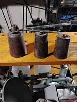 Top side view of 3 cast iron vintage scale weights on a wooden surface showing metal loops and hook attachment.