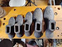 Top view of five cast iron cobbler shoe lasts in different sizes placed on a workbench