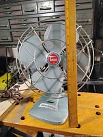 Side angled view of vintage electric fan showing motor electric label and metal blade.