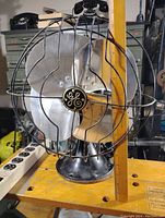 Front left three-quarter view of fan showing GE medallion, blade design and wire guard