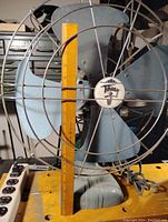 Front view showing entire vintage fan with metal blades, wire cage, and base with power cord. Ruler placed beside fan blade showing blade size approximately 12 inches.