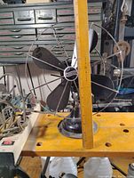 Front view showing the 4 black blades, wire cage, and center Air King badge with ruler for scale showing fan approx 14-15 inches tall.