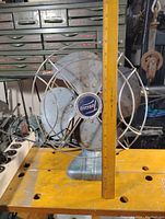 Front view of vintage Tocecni electric fan showing metal blades and protective wire cage with mounted ruler indicating size.