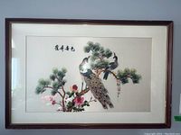 Wide view of one framed embroidered artwork showing two peacocks on a pine branch with pink flowers, Asian script in the top left, matted and framed under glass.