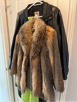 Fox fur coat in natural brown and orange hues with thick fur, hanging in front of black leather jacket and dark winter coat.
