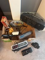 Overview of electronics and small appliances in a box including radios, clock radios, curling irons, and hand fans
