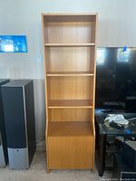Photo of a tall wood veneer rectangular shelf unit with three open shelves and closed cabinet at bottom