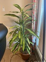 Full view of the faux plastic plant showing the tall leaves and brown pot from an angle