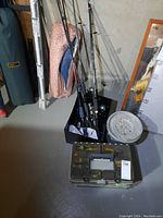 Full view of fishing rods in black bin, tackle box in front, and metal bait container on floor