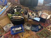 Image showing multiple boxes containing various cables, a WD TV box, remote controls, an auxiliary speaker, and other miscellaneous electronic items on a carpet.