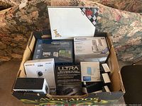 Box showing multiple electronics including Magellan GPS box, Panasonic cordless phone box, and other electronic devices with packaging